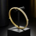 Minimalist Lustre Line 18k gold bangle encrusted with three rows of diamonds, displayed on a black jewelry stand.