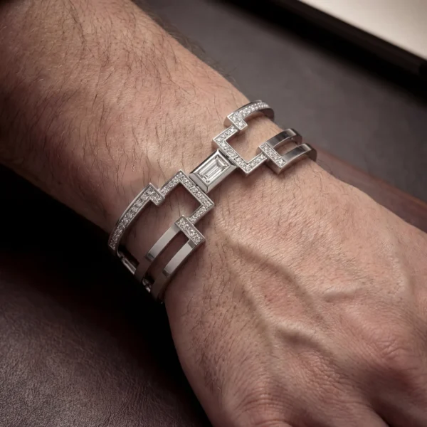 A close-up of a man's wrist wearing a wide, geometric silver bracelet set with sparkling diamonds.