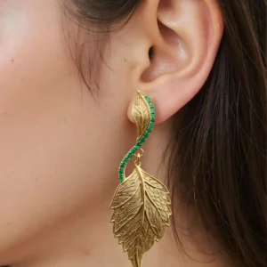 Macro close-up of gold leaf-shaped earrings featuring green emerald detail.