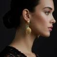 Woman wearing gold leaf earrings with emerald stones against a dark background.