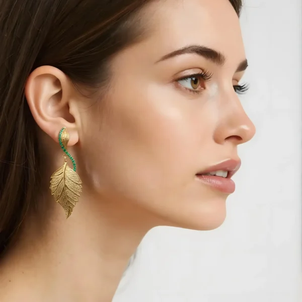 Profile view of a woman wearing gold leaf earrings with emerald accents.