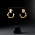 Twisted gold hoop earrings with textured silver studs on a black stand.
