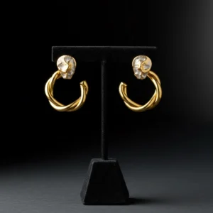 Twisted gold hoop earrings with textured silver studs on a black stand.