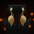 Pair of gold Emerald Whisper leaf earrings on a black jewelry stand.