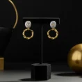 Golden Twirl hoop earrings with textured silver studs on a black stand.