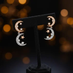 Moon and star drop earrings with silver and rose gold finishes on a black stand.