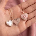 Close-up of a woman wearing an open rose gold heart locket with an engraving.