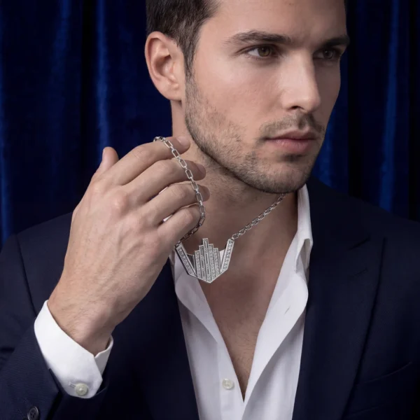 Close-up of man holding silver skyline pendant chain.