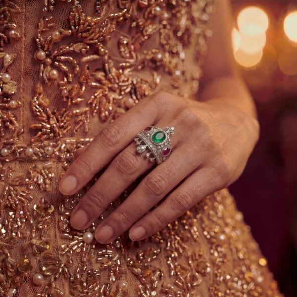 Sovereign crown ring with emerald and rubies on finger.