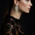 Side view of a woman wearing silver chandelier earrings with emerald droplets.