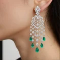 Macro shot of silver chandelier earrings featuring green emerald teardrops.