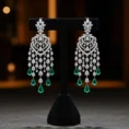 Silver Victorian Glow chandelier earrings with emerald accents on a black stand.