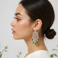 Profile view of a woman wearing intricate silver and emerald drop earrings.