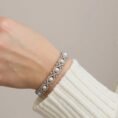 Close-up of a woman wearing the Oasis of Elegance pearl and diamond bracelet with a white sweater.